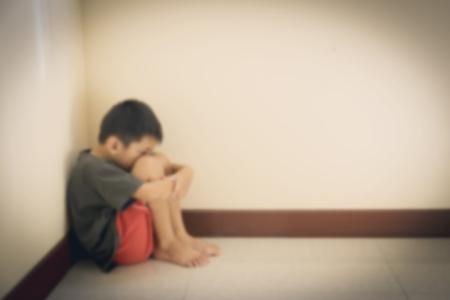 Blurred of the boy hugged her knees in tears in a corner of the room.の写真素材