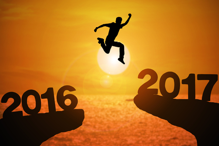 Silhouette of young man jumping between 2016 and 2017 years with beautiful sunset at the sea.の写真素材