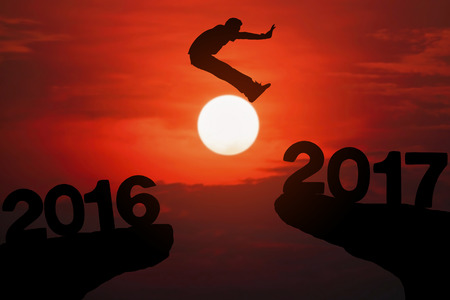 Silhouette of young man jumping between 2016 and 2017 years with beautiful sunset.の写真素材