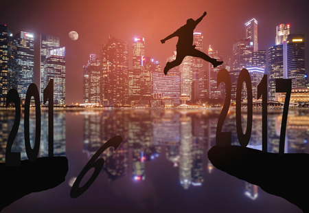 Silhouette of young man jumping between 2016 and 2017 years with beautiful city background.の写真素材
