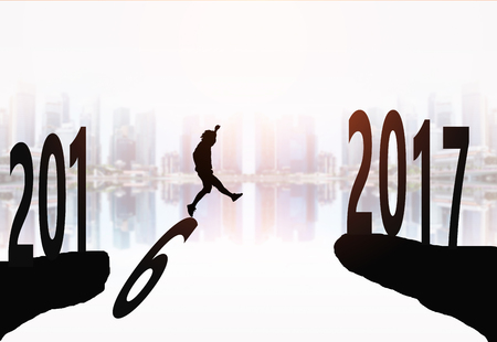 Silhouette of young man jumping between 2016 and 2017 years with beautiful city background.の写真素材