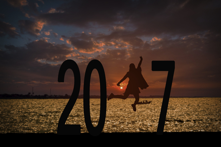 Silhouette of young woman jumping on the beach between 2017 years with beautiful sunset at the sea.の写真素材