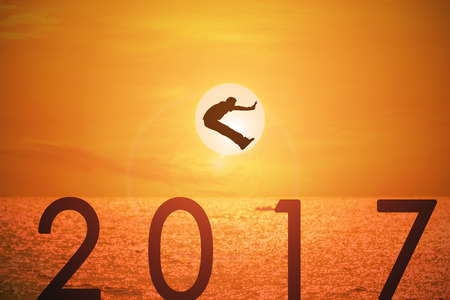Silhouette of young man jumping over the numbers 2017 years with beautiful sunset at the sea.の写真素材