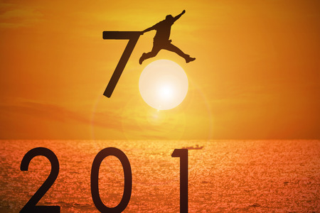 Silhouette of young man jumping over the numbers 2017 years with beautiful sunset at the sea.の写真素材