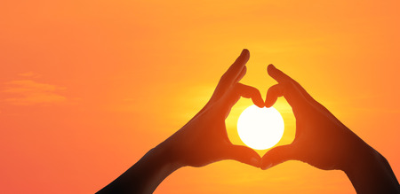 Panorama silhouette of female hands making a heart shaped symbol with beautiful sunset background.の写真素材