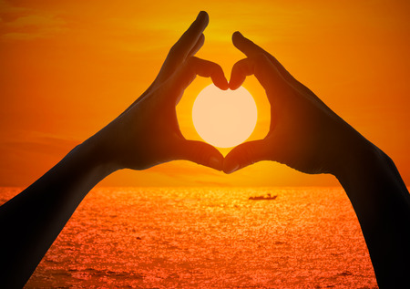 Silhouette of female hands making a heart shaped symbol with beautiful sunset background.の写真素材