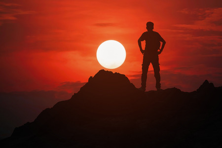 Silhouette of young man standing on the top of the mountain with beautiful sunset background, concept for success and victory.の写真素材