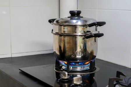 A stainless steel pot is placed on a gas stove that is turned on for cooking in the kitchen.