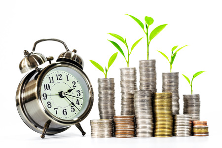 Trees are growing on a pile of coins with a clock over white background. Concepts of business, money saving and business growth.の写真素材