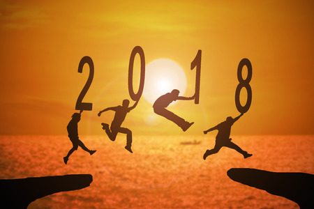 Silhouette group of young mans jumping between 2017 and 2018 years with beautiful sunset at the sea-use for news year and concepts for business and target.の写真素材