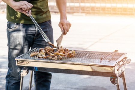 One man is grilling pork on a barbecue grill made of stainless steel.の写真素材