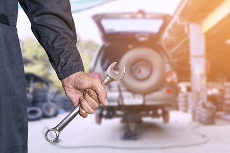 Car repairman wearing a dark blue uniform standing and holding a wrench that is an essential tool for a mechanic and has a backdrop as a car repair center.の写真素材