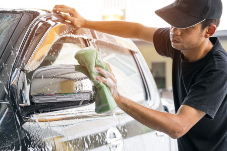 Car wash worker wearing a T-shirt and a black cap is using a sponge to clean the car in the car wash center, concept for car care industry.の写真素材
