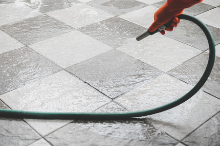 Hand of man wearing orange rubber gloves is use a hose to clean the tile floor.の写真素材