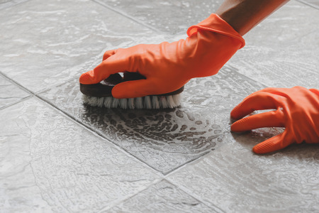 Hand of man wearing orange rubber gloves is use a hose to clean the tile floor.の写真素材