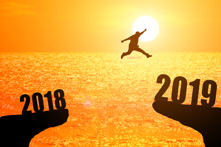Silhouette of young man jumping between 2018 and 2019 years with beautiful sunset at the sea-concepts of news year and business target.の写真素材