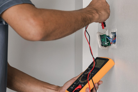 Electrician is using a digital meter to measure the voltage at the power outlet in on the wall.の写真素材