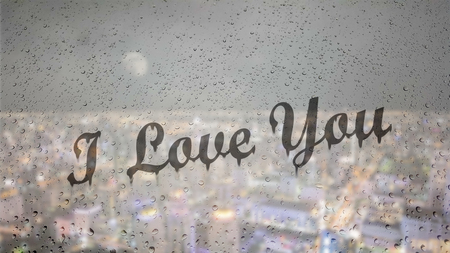 Draw letters I love you by hand on a glass with water drops droplets with night cityscape background.の写真素材