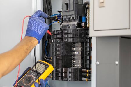 Electrician is using a digital meter to measure the voltage at the circuit breaker control cabinet on the wall.の写真素材