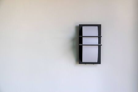 Close-up of a modern design of a wall mounted house lighting on white cement walls.