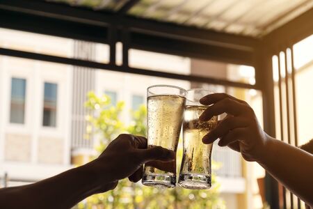 The hands of two men holding a glass of beer raised together to drink to celebrate the success.の写真素材
