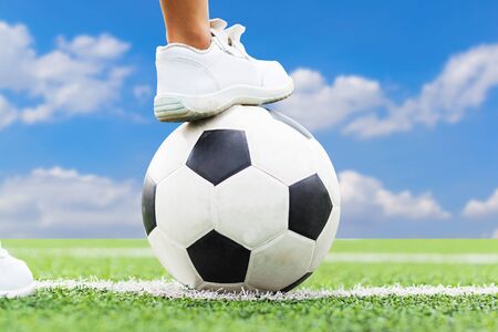 Feet of a boy wearing white sneakers stepping on a soccer ball in the middle of the football field.の写真素材
