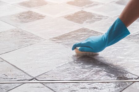 Hand of man wearing blue rubber gloves is used to convert scrub cleaning on the tile floor.の写真素材