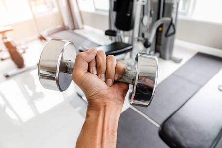Closeup a man's hand holds a dumbbell with his left hand in the gym, Concept for exercise and health care.の写真素材
