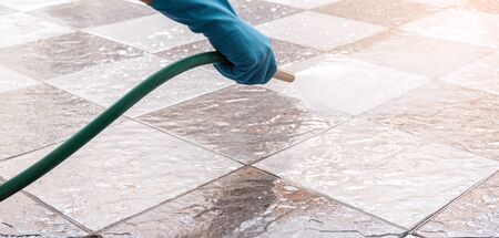 Hand of man wearing blue rubber gloves using a hose to cleaning the tile floor.の写真素材