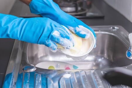 Close up of a man wearing a blue rubber glove was washing the cup with a dish washing liquid in the sink in the kitchen.の写真素材