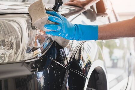 Car wash staff wearing blue rubber gloves using a sponge moistened with soap and water to clean the car.の写真素材