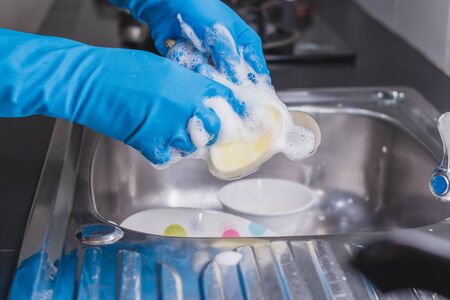 Close up of a man wearing a blue rubber glove was washing a spoon with a dish washing liquid in the sink in the kitchen.の写真素材