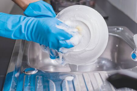 Close up of a man wearing a blue rubber glove was washing the cup with a dish washing liquid in the sink in the kitchen.の写真素材
