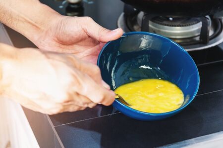Close men's hand using a spoon beat the eggs in a ceramic cup to cook.の写真素材