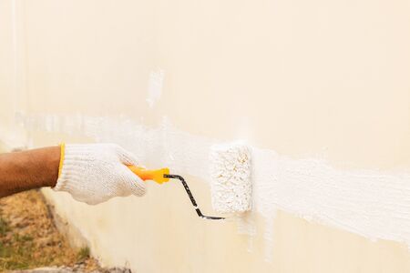 Closeup on hand wearing white cloth gloves, using a roller for painting white color on the concrete wall.の写真素材