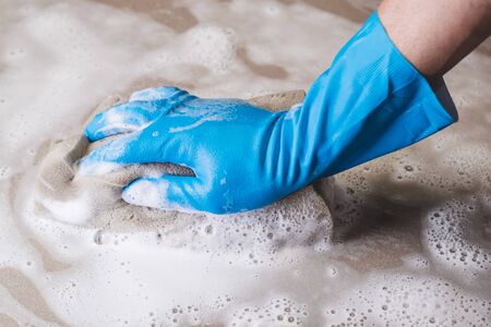 Hand of man wearing blue rubber gloves is using a sponge cleaning the tile floor.の写真素材