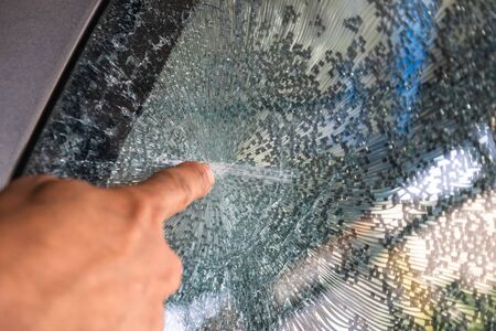 Man's hand pointed to the crack of the windshield caused by an accident on the road.の写真素材