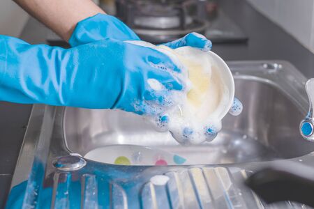 Close up of a man wearing a blue rubber glove was washing the cup with a dish washing liquid in the sink in the kitchen.の写真素材