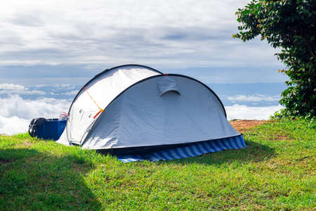 Closeup a camping tent that is set up on a grass field at the highest point of a high mountain with a backdrop of sky and clouds.の写真素材