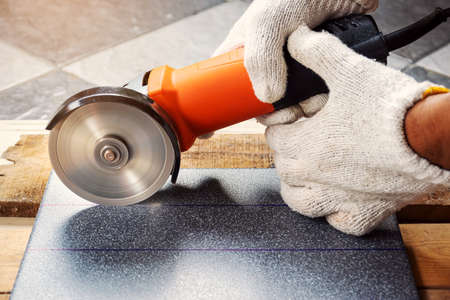 Construction worker wearing white cloth gloves was cutting the tiles with an electric grinder.の写真素材