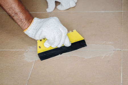 Construction worker in white gloves is working to grout the tiles in the bathroom.の写真素材