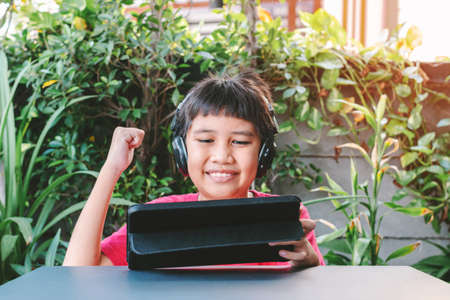Asian cute boy wearing wireless headphones and smiling happily while playing games on the tablet.の写真素材