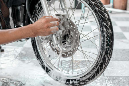 Close-up of a man's hand washing a motorbike's wheels with sponges and bubbles.の写真素材