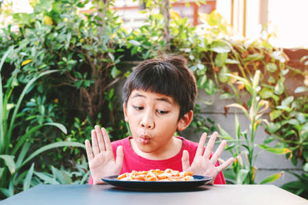 Cute Asian child in a red shirt showed a good expression when he saw a pizza in a plate placed in front of the table.の写真素材