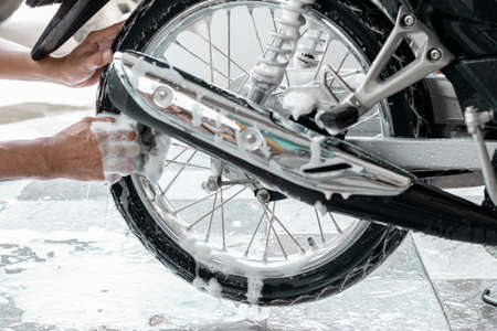 Close-up of a man's hand washing a motorbike's wheels with sponges and bubbles.の写真素材