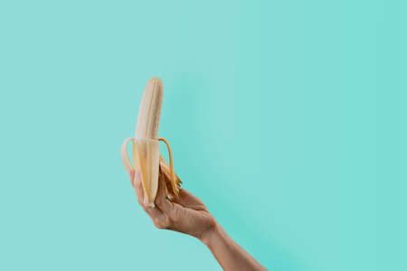 Closeup a woman's hand holding a ripe banana isolated on green pastel colors backgroundの写真素材