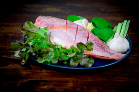 Closeup a fresh fish and vegetables in ceramic dishes prepared for cooking.