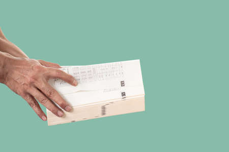Hand holding and opening a thick book isolated on green pastel color background.の写真素材