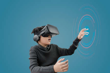 Asian boy wearing VR glasses headset with technology graphics in front on blue color background.の写真素材