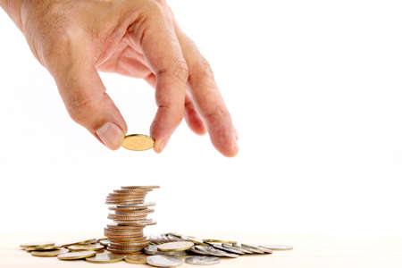 Closeup of human hand putting a coin on a pile of coins, use for business and finance concepts.の写真素材